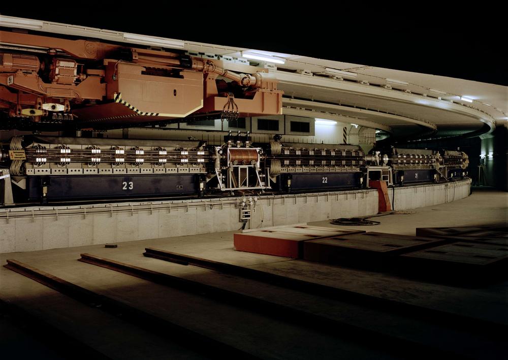 Historisches Foto. Es zeigt eine Kurve im Tunnel des Ring-förmigen Teilchenbeschleunigers DESY. Wände aus Beton und Aufbauten aus Stahl zeichnen den Gesamteindruck aus.